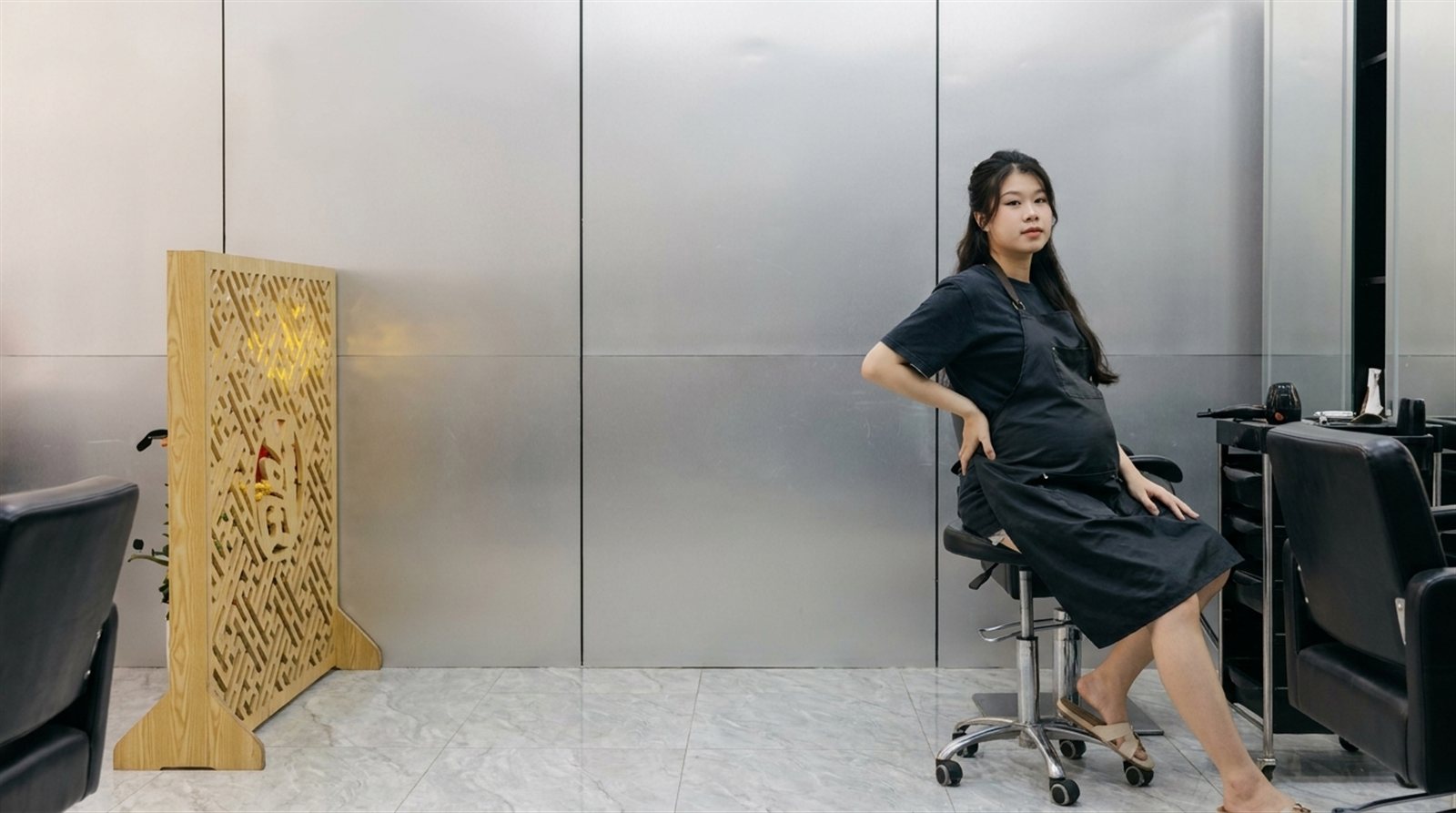 Thợ tóc nữ mang thai ngồi nghỉ trên ghế cao giữa ca làm tại salon Nhật Tâm