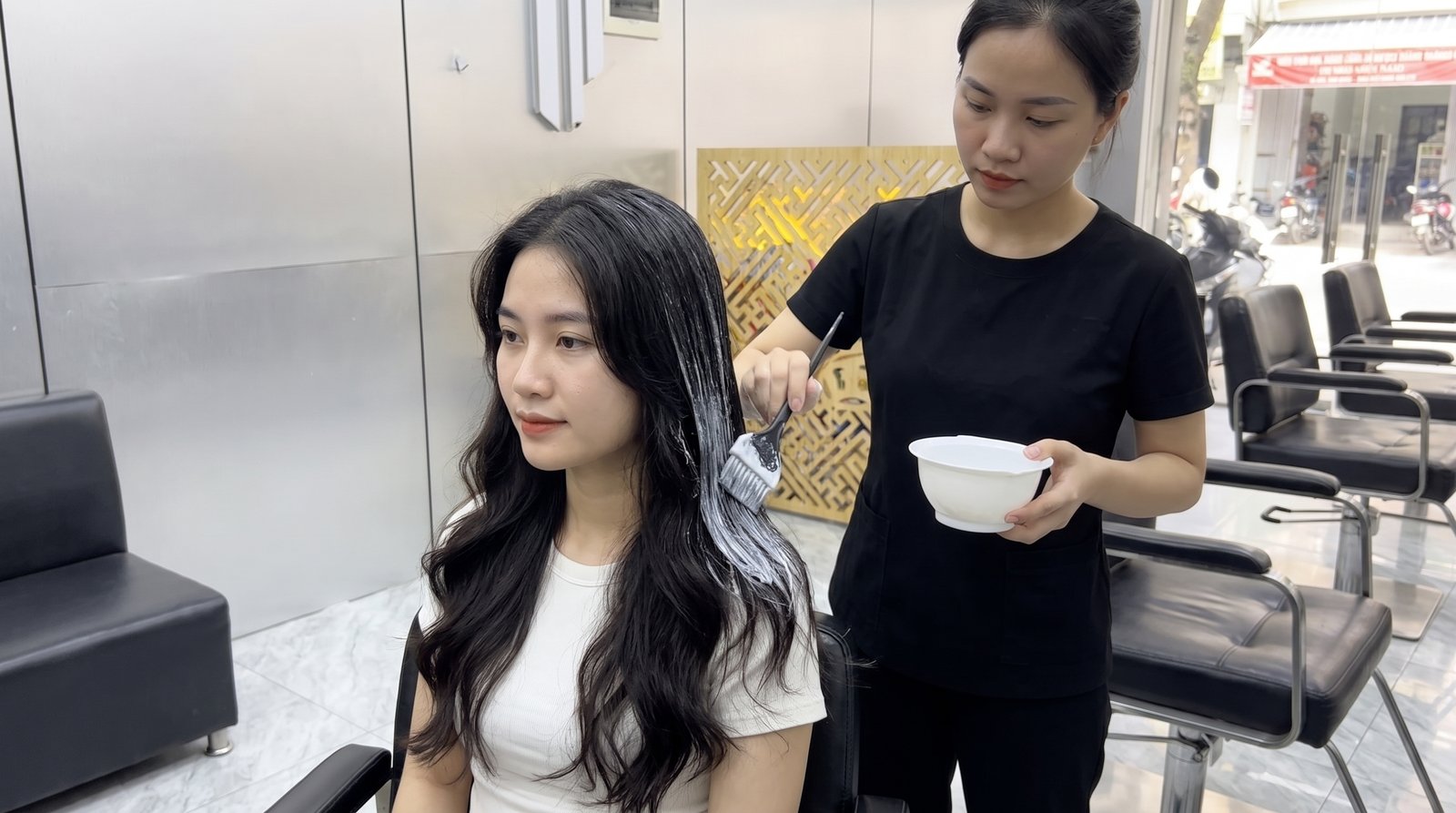 Thợ tóc thoa kem ủ tóc bằng cọ cho khách tại Nhật Tâm Hair Salon