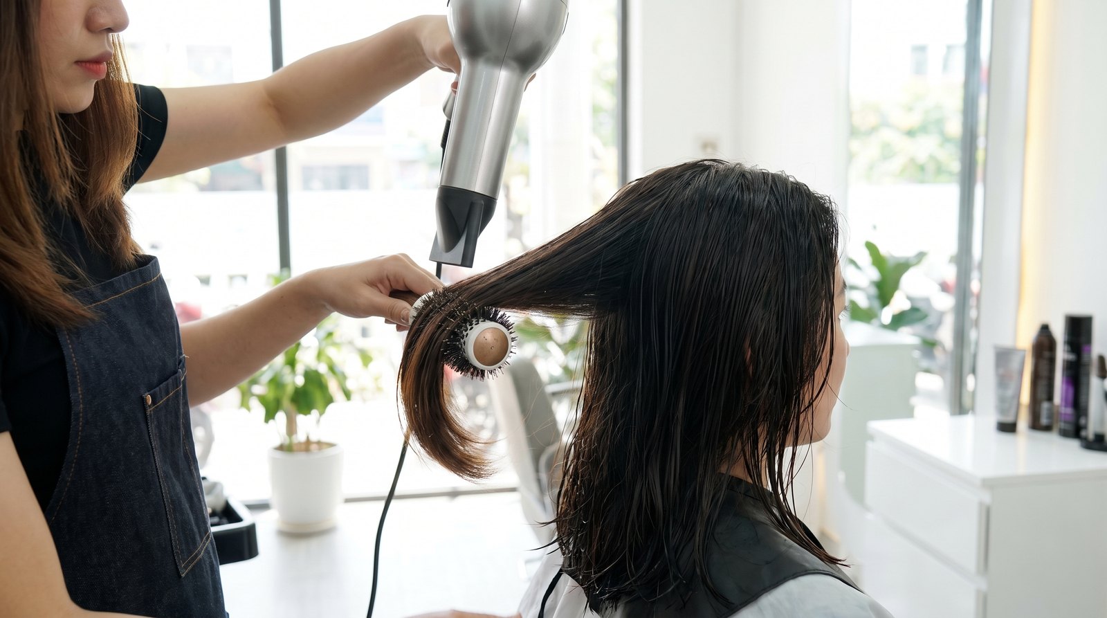 Stylist dùng lược tròn kéo cụp đuôi tóc ngắn khi sấy để tóc hết vểnh