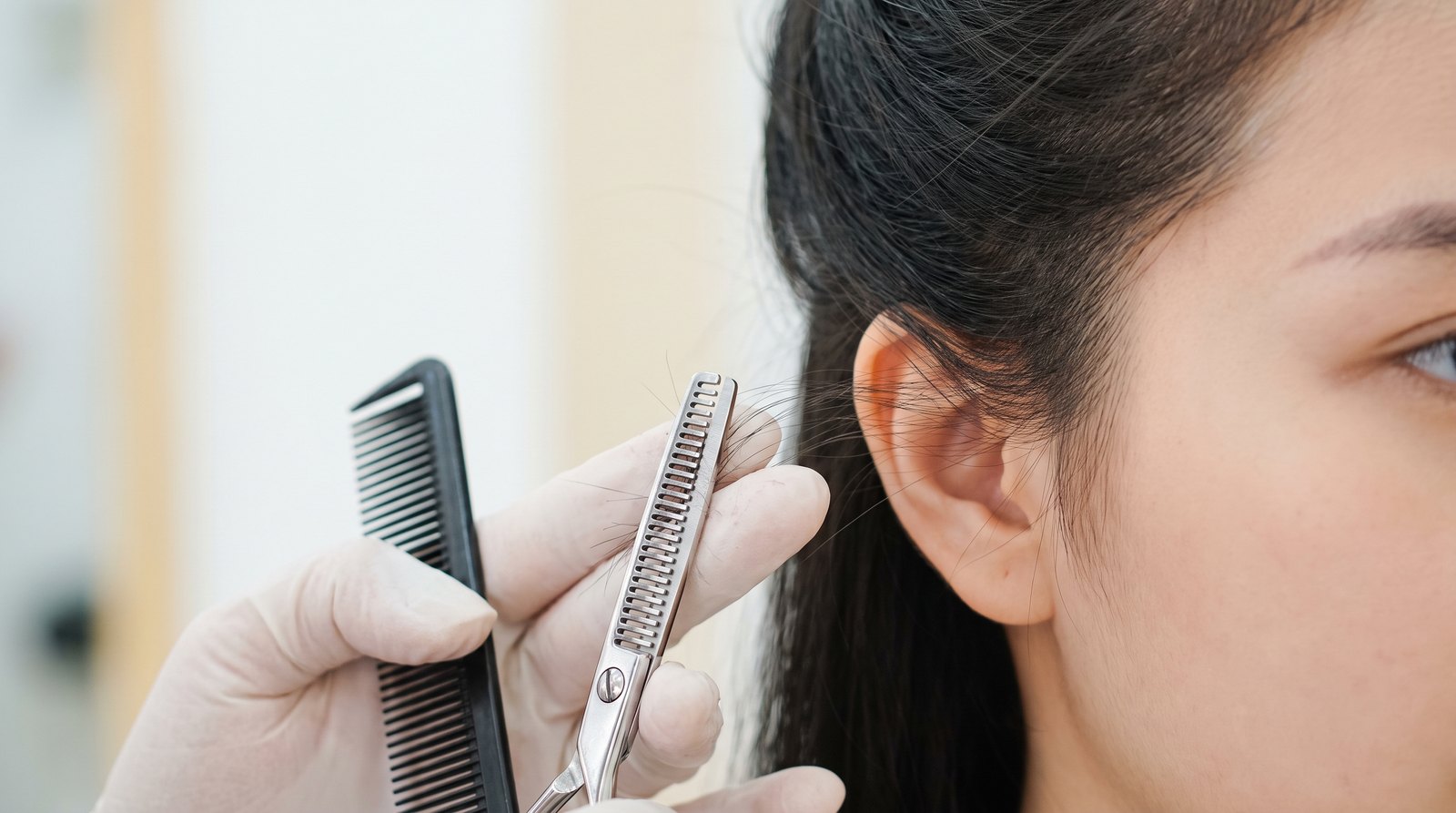 Thợ tóc dùng kéo tỉa thưa phần tóc mai trước vành tai cho khách nữ