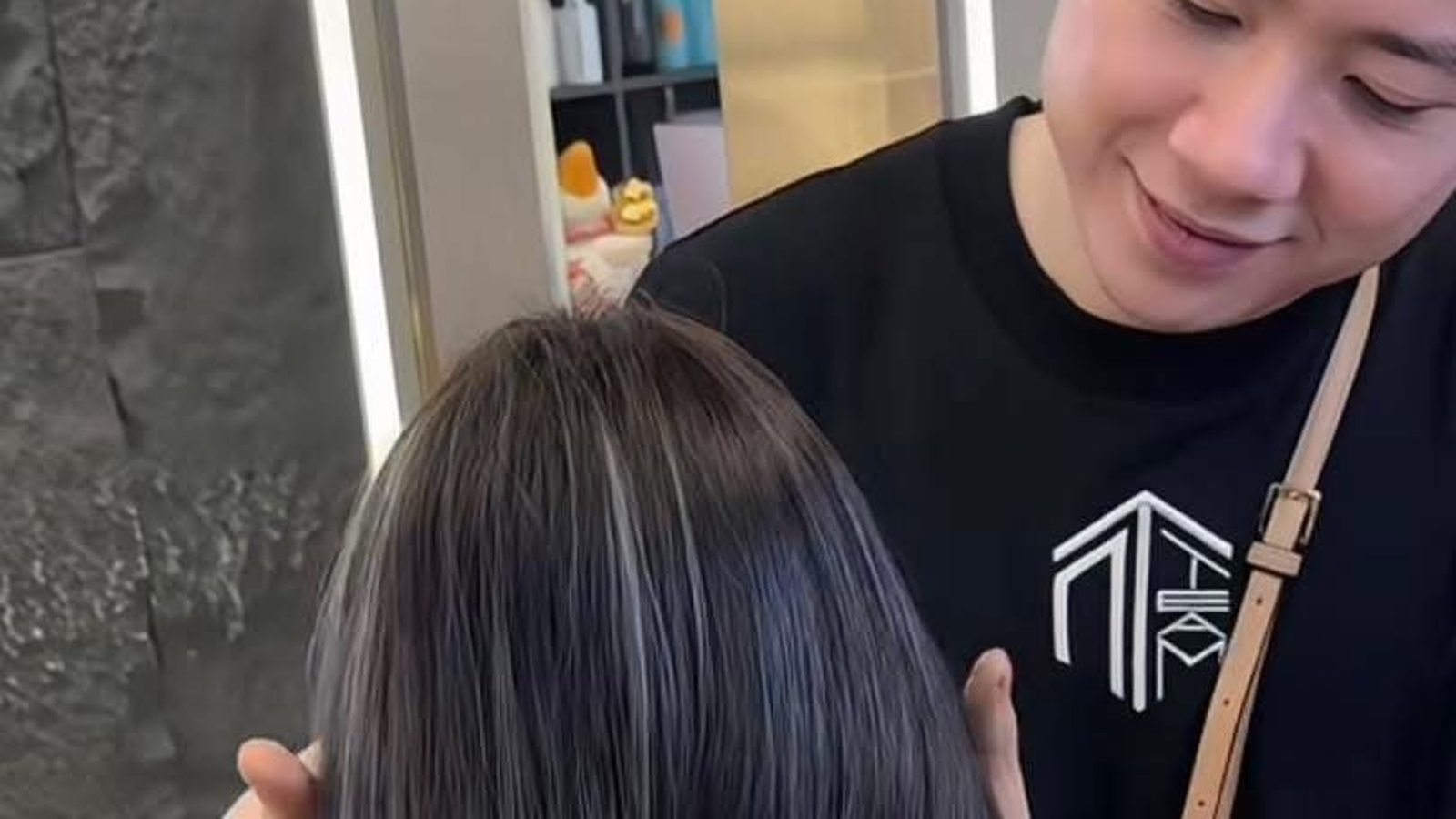 Stylist at Nhat Tam Hair Salon in Hanoi lifting a section of dark hair with fine ash streaks to check how evenly the color has taken